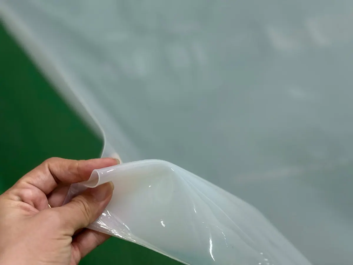Tay nhấc mép tấm silicone mỏng trên bàn xanh